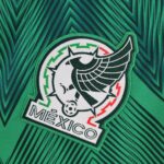 Close-up of green fabric with a textured chevron pattern and a white circular embroidered patch partially visible in the corner.
