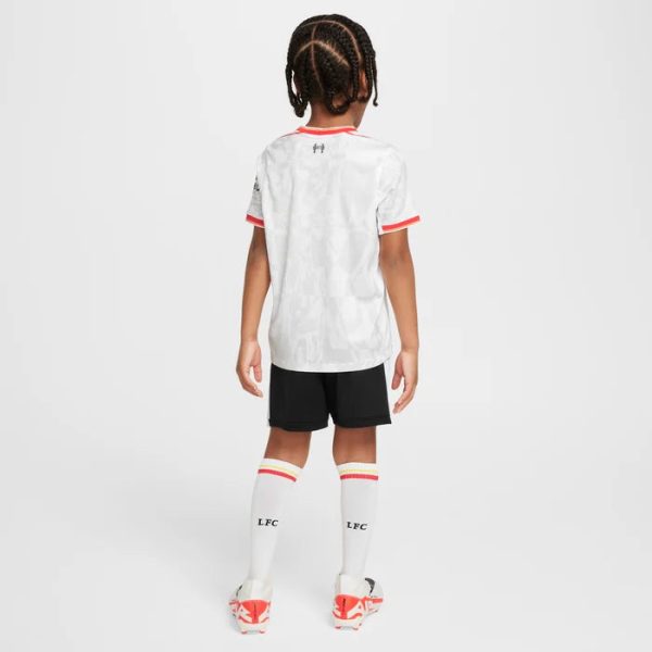 Child wearing a white jersey with red trim, black shorts, white knee-high socks with 'LFC', and red-and-white soccer cleats, seen from the back.