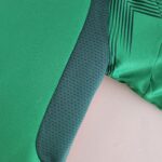 Close-up of green fabric with a dark gray textured strap crossing diagonally over a pale pink background.