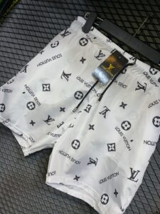 White Louis Vuitton shorts with black LV logos and a hanging brand tag on a black rack surface