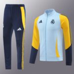 Navy track pants with yellow side stripes paired with a light blue and yellow Real Madrid jacket featuring the club crest and Adidas logo on the chest.