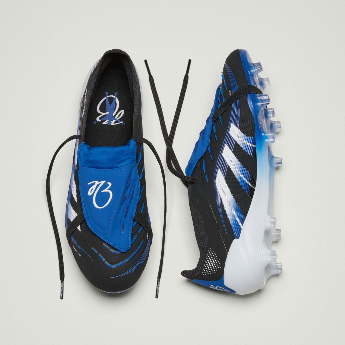 Blue and black soccer cleats with white stripes, laces untied, viewed from above on a light background.