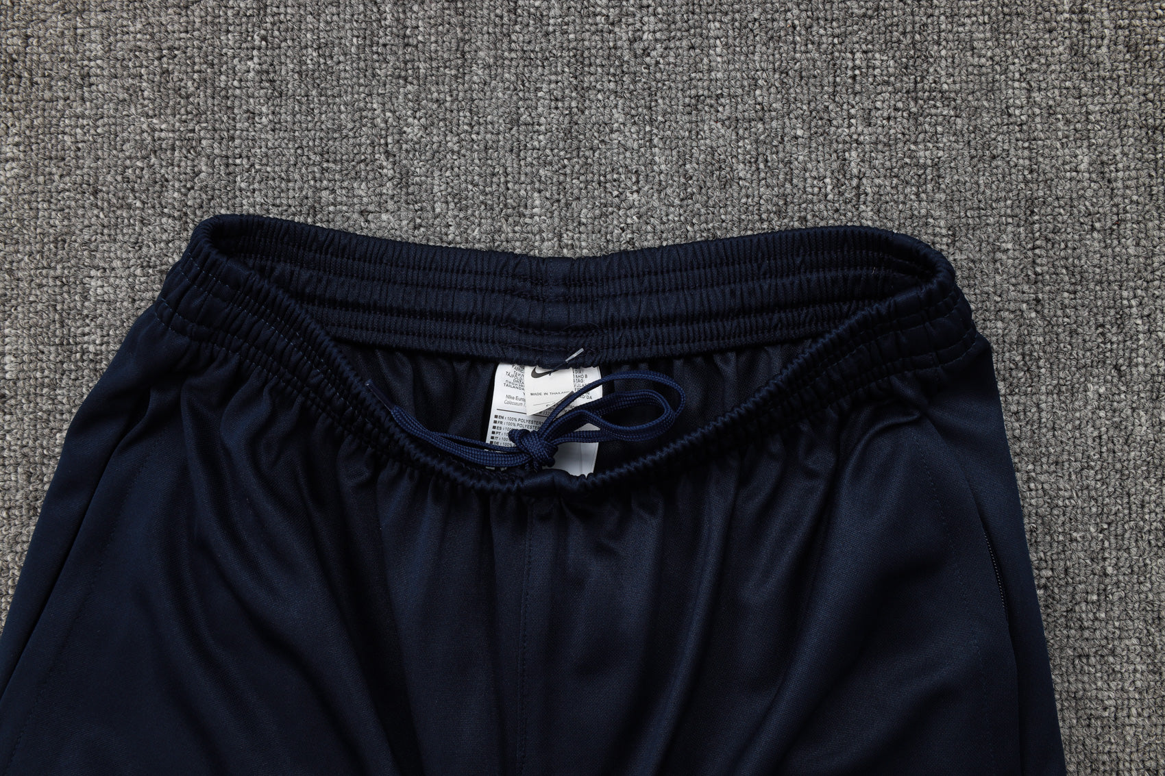 b2fb6097 | UAE SPORT STORE Navy blue pants with an elastic waistband and drawstring on a gray carpet, tag visible between the fabric edges.
