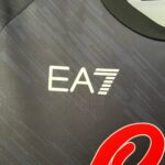 Close-up of dark fabric with a partial white logo and a red curved graphic in the bottom-right corner.