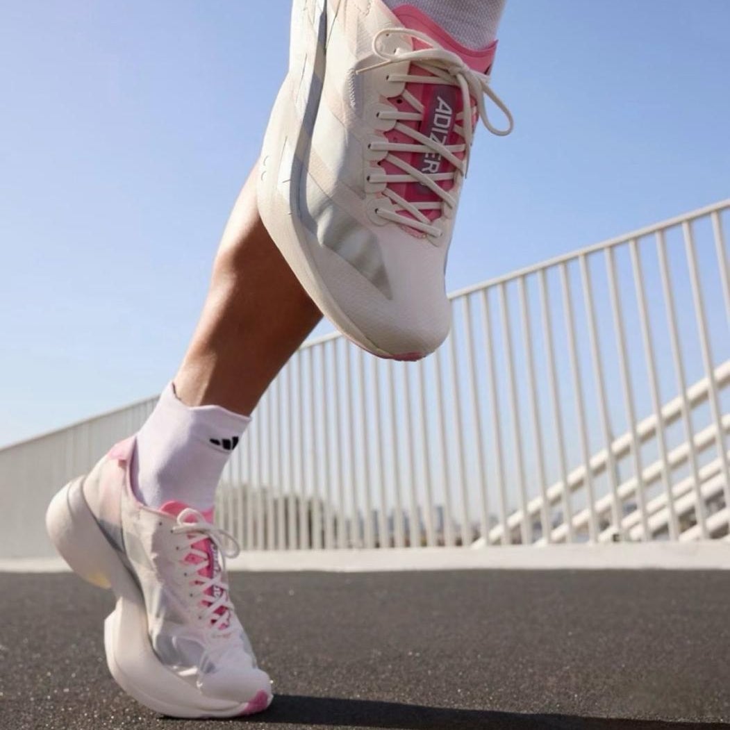 b3278535-c1ec-4a89-ace3-354a7a35c703 Close-up of white and pink athletic shoes in mid-step on a paved path with a railing in the background