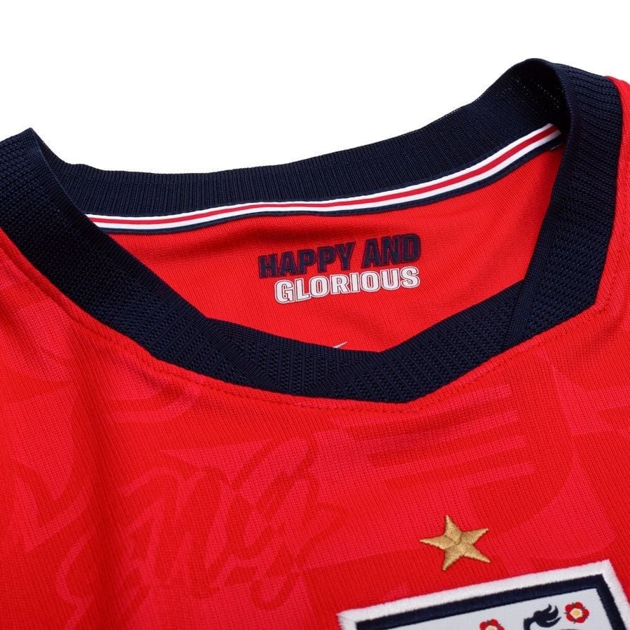b3631d505217 | UAE SPORT STORE Close-up of a red sports jersey collar with navy trim; label reads 'HAPPY AND GLORIOUS' and a small gold star patch nearby