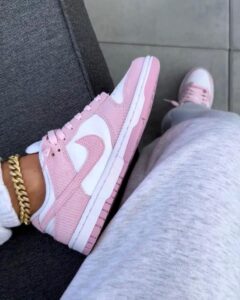 Light pink and white Nike sneakers with white midsole, worn with gray joggers and a gold chain bracelet visible at the ankle.