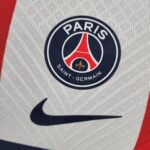 Close-up of a Paris Saint-Germain crest patch on light gray fabric with a red stripe.