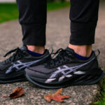 Close-up of black and gray running shoes on a person standing on a concrete path with autumn leaves nearby. (informative footwear image)",