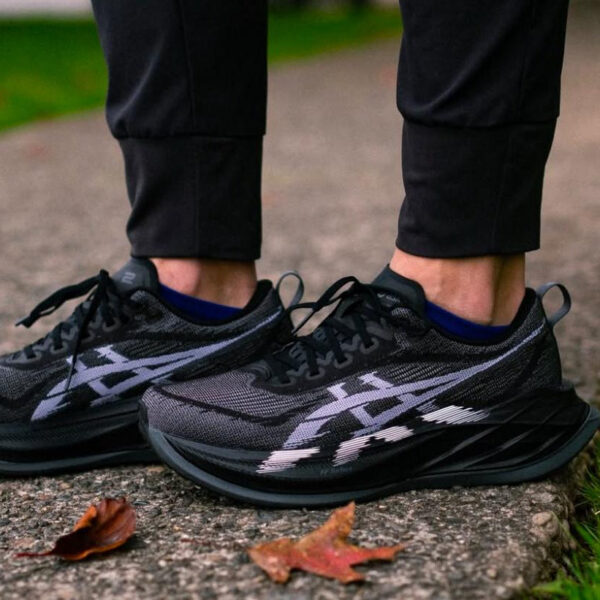 Close-up of black and gray running shoes on a person standing on a concrete path with autumn leaves nearby. (informative footwear image)",