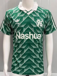 Green soccer jersey with geometric chevron pattern, white collar, sponsor text 'Nashua' across the chest and Adidas logo on the left; a white circular emblem with '96' on the right.