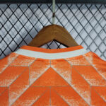 Orange geometric-patterned shirt on a wooden hanger against a metal grid background.