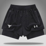 b49be0ba | UAE SPORT STORE Black athletic shorts with elastic waistband, zip pockets, and white logos on each leg (Under Armour on the right, bull head on the left).