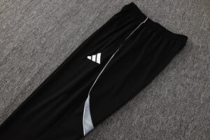 Black athletic joggers with white piping and a small Adidas logo on the thigh, laid flat on gray carpet