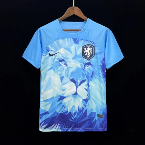 Blue soccer jersey with geometric lion design, Nike swoosh, and crest on the chest, hanging on a wooden hanger against a black background.
