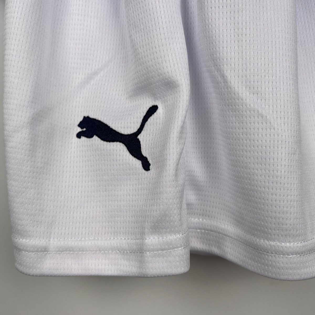 Close-up of white textured fabric with a small dark navy Puma logo visible on the left.