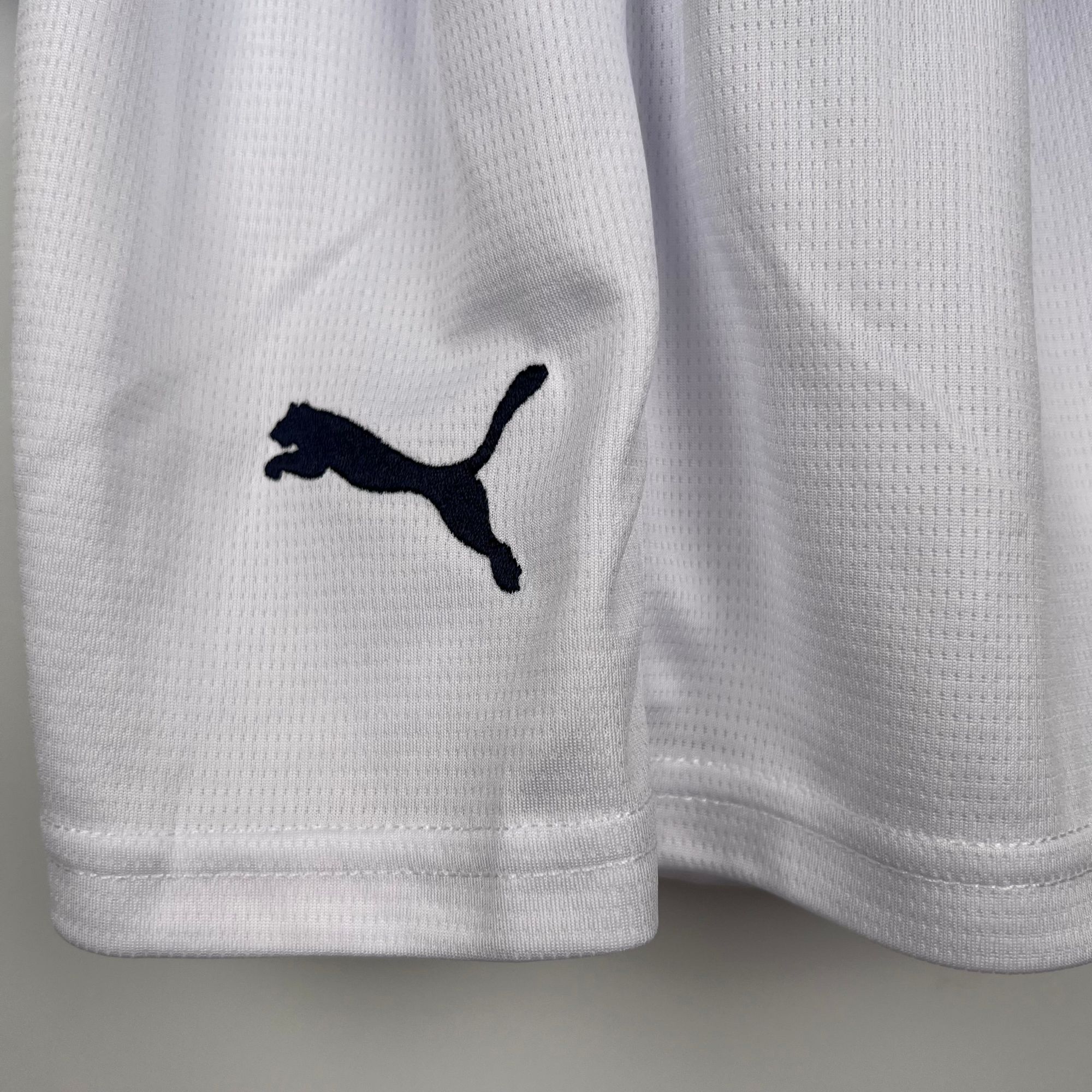 b5480d6e_62087792-fd34-49ce-9a46-30405a048fbe | UAE SPORT STORE Close-up of white textured fabric with a small dark navy Puma logo visible on the left.