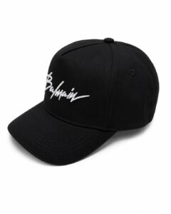 Black baseball cap with white embroidered cursive logo on the front (reads Balmain)