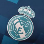 b590a0c1_ba179299-a564-4e98-94b9-e62f277dea30 | UAE SPORT STORE Close-up of a teal crown sticker on dark blue fabric.
