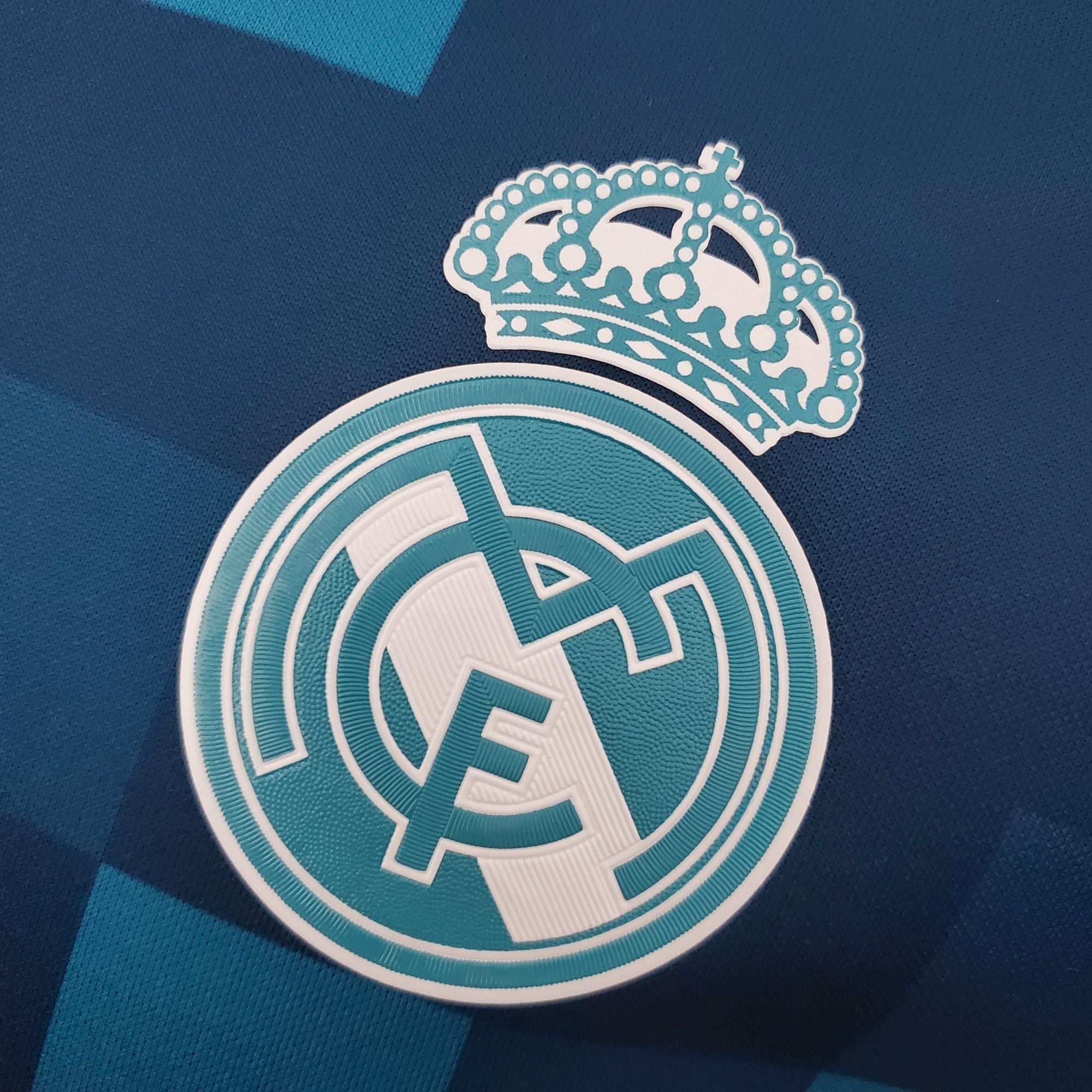 b590a0c1_ba179299-a564-4e98-94b9-e62f277dea30 | UAE SPORT STORE Close-up of a teal crown sticker on dark blue fabric.