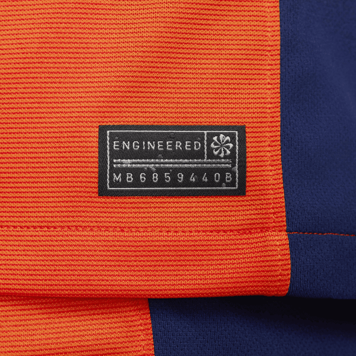 b5c2c792_a8d0_4a64_9b4e_733ec69a078c | UAE SPORT STORE Tag on an orange fabric reading 'ENGINEERED' with a small star symbol and serial MB685940B on a blue background image of a clothing item.