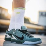 Close-up of teal Nike basketball sneaker with black swoosh on a white sock, standing outdoors on a sunny day.