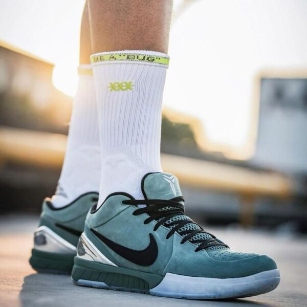 Close-up of teal Nike basketball sneaker with black swoosh on a white sock, standing outdoors on a sunny day.