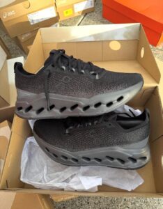 Pair of black running shoes with a perforated knit upper and distinctive hollow midsole, inside an open shoebox.