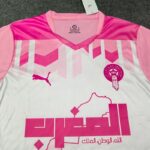 Pink and white soccer jersey with geometric pink pattern, Puma logo on the left chest, circular Moroccan emblem on the right chest, and the Arabic motto Allah, al-Watan, al-Malik across the bottom.
