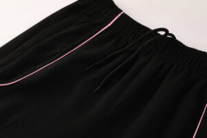 b64b0118 | UAE SPORT STORE Close-up of black jogger pants with pink piping along the pocket seam and a drawstring elastic waist.