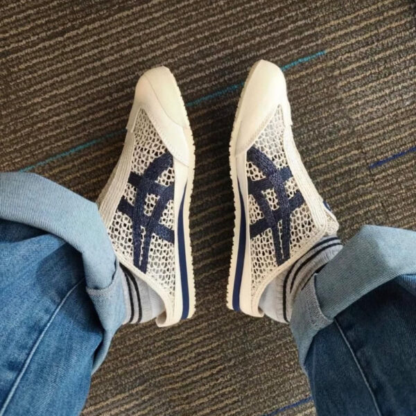 Top-down view of a person wearing white mesh sneakers with navy branding, standing on a brown carpet with cuffed blue jeans.