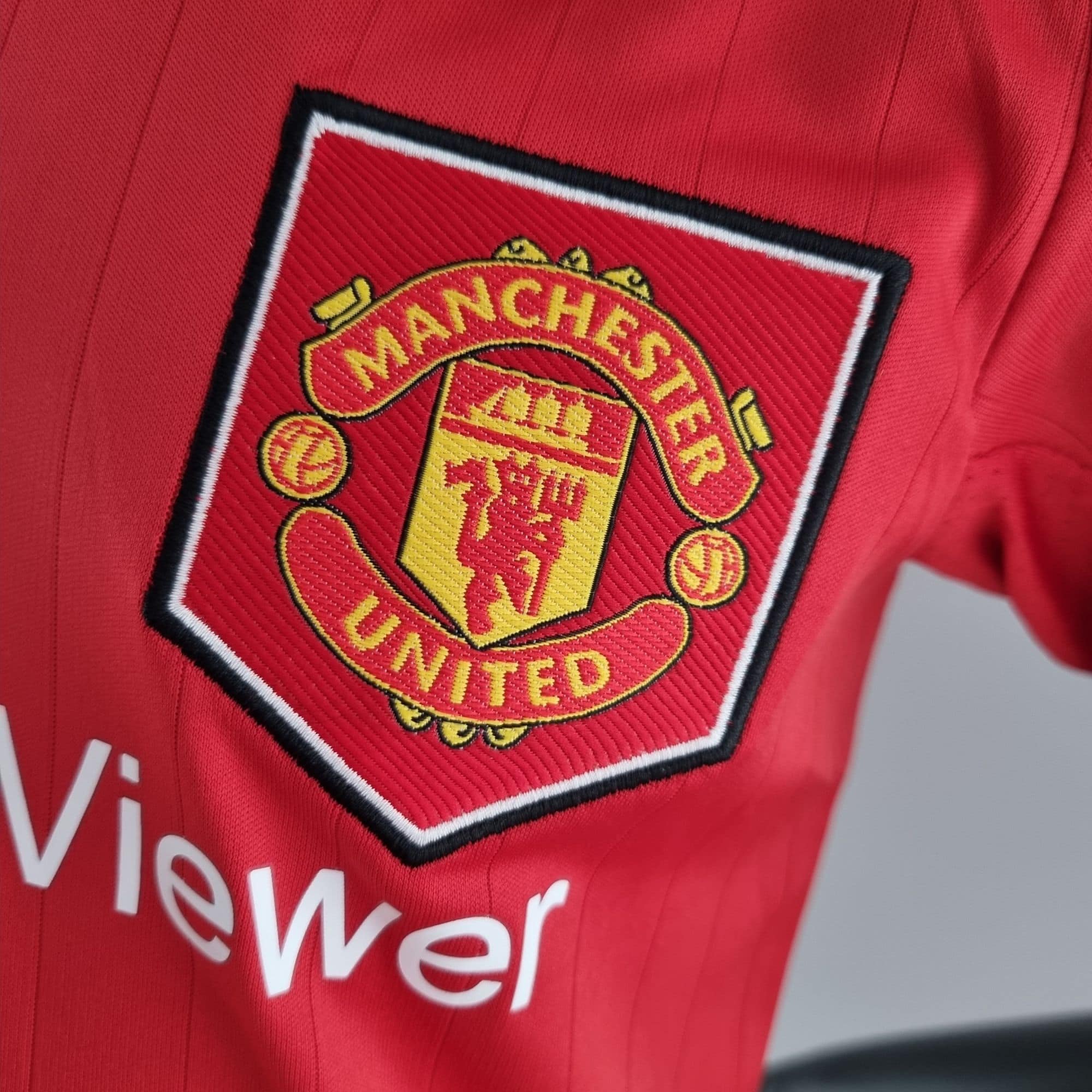 b71eb726_e1561f31-2f1a-4bd8-a1db-8922cfbddb9e | UAE SPORT STORE Close-up of a red fabric jacket featuring the embroidered Manchester United crest.