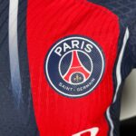 Close-up of a Paris Saint-Germain football jersey showing a red stripe and the circular club badge.