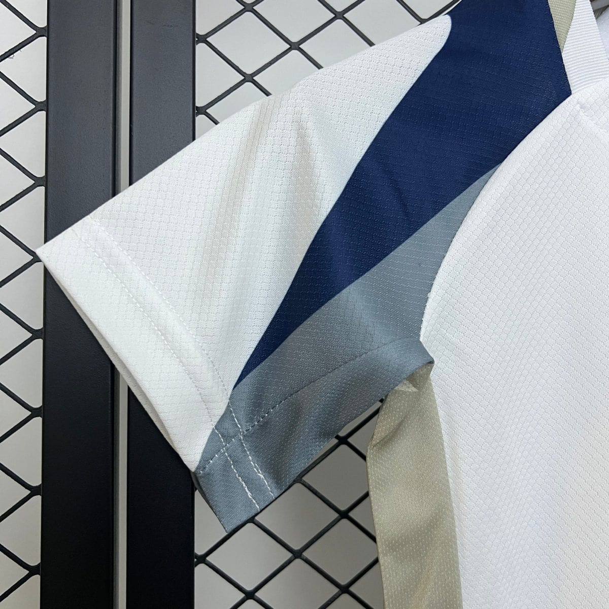 Close-up of a chain-link fence with dark vertical bars and overlapping white, blue, and beige fabric strips draped over it.