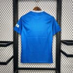 Blue athletic jersey hanging on a wooden hanger against a black metal rack, viewed from the back with a white-striped collar.