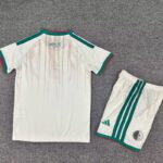 White soccer kit consisting of a short-sleeve jersey and matching shorts, with green and red trim and Arabic text on the back of the jersey; shorts have green stripes and a small circular emblem near the hem.