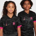 b8191edc_81cf_489d_8a5e_216d439adb0f | UAE SPORT STORE Two young girls in matching black soccer jerseys with pink accents, standing side by side for a team photo.