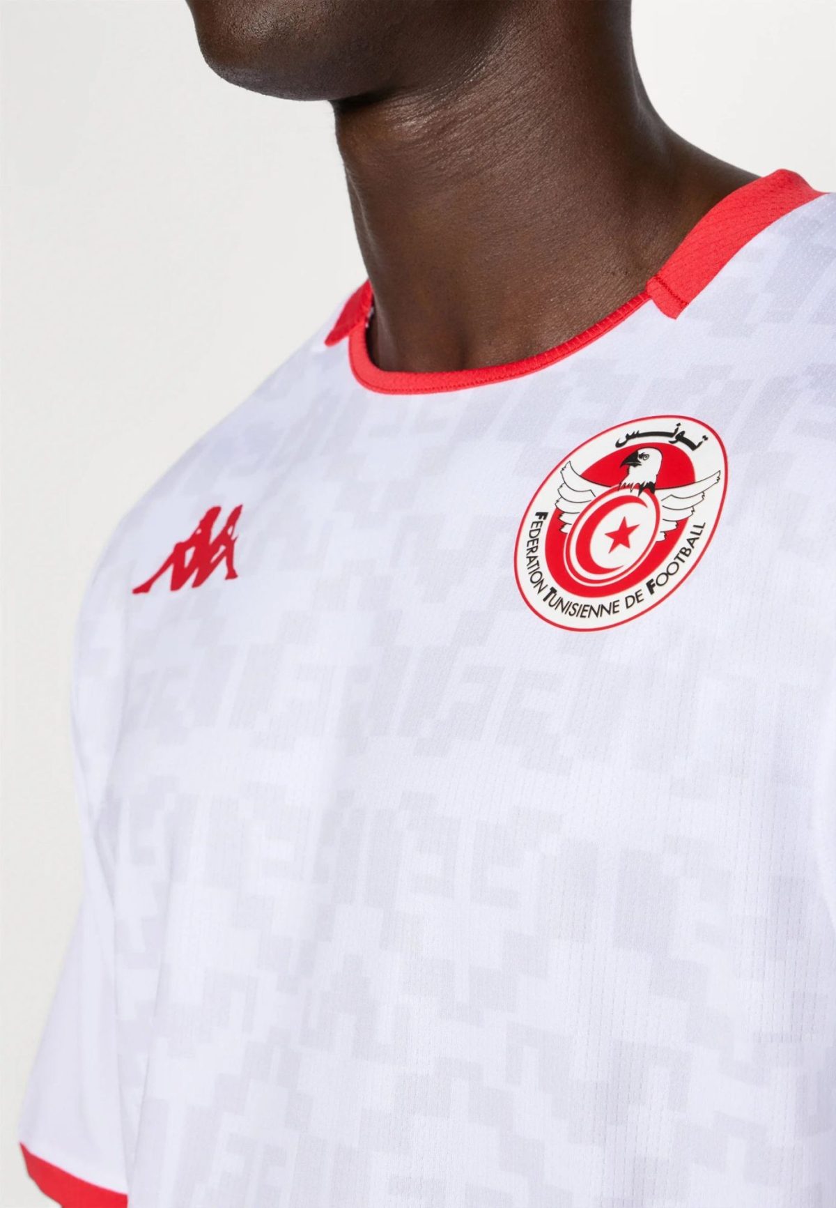 Close-up of a dark-skinned athlete wearing a white jersey with red trim and the Tunisian Football Federation crest on the chest.