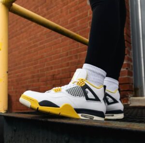 White and yellow sneakers with black accents resting on a dark metal ledge beside a brick wall, worn with white crew socks