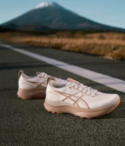 Pair of white and peach running shoes on an asphalt road with a distant mountain in the background.