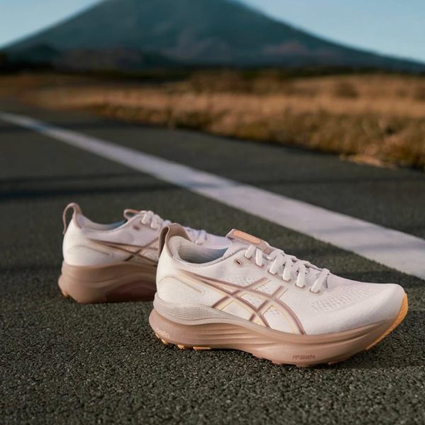 Pair of white and peach running shoes on an asphalt road with a distant mountain in the background.