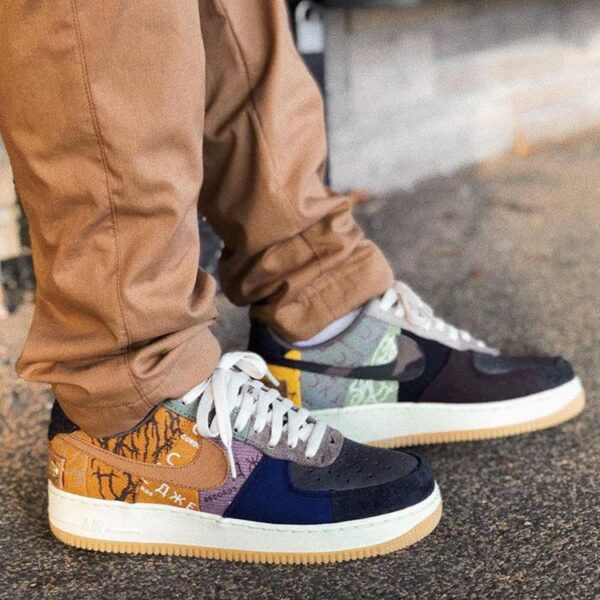 Close-up of colorful patchwork sneakers with white laces on a person wearing tan pants, standing on pavement