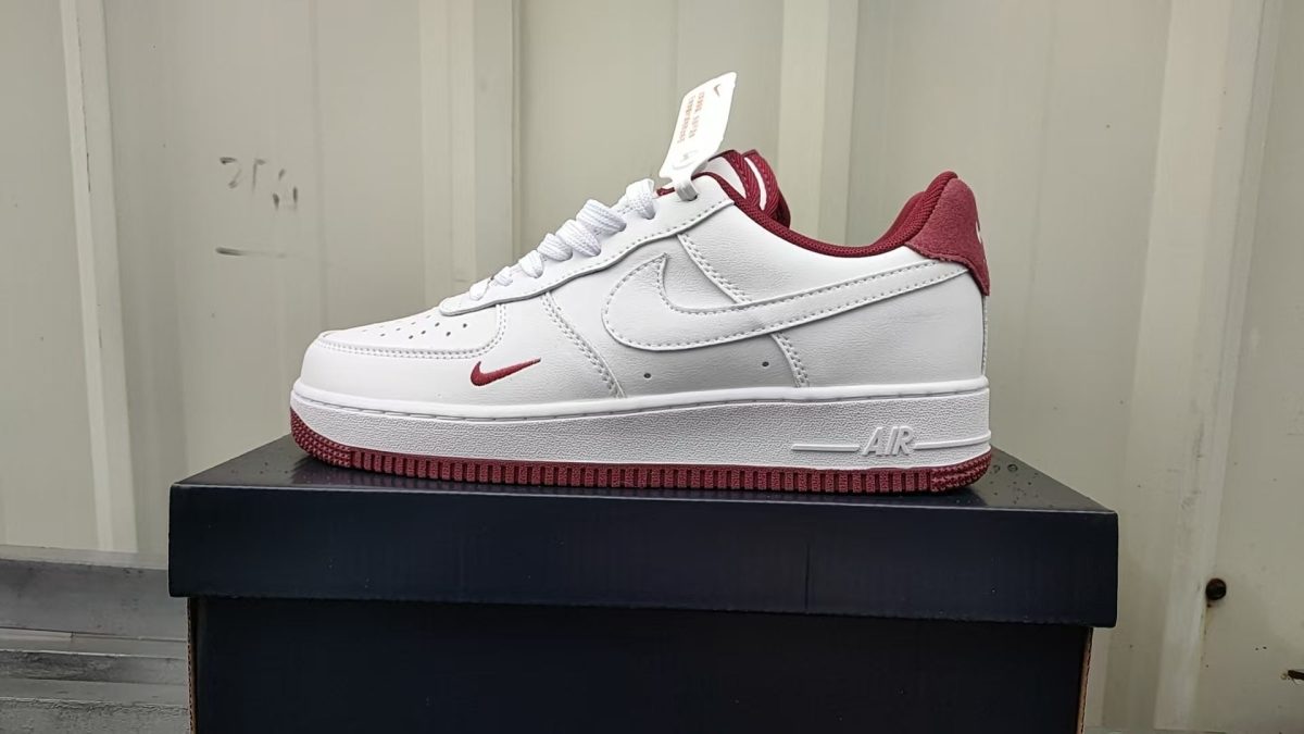 White Nike Air Force 1 sneaker with red accents on a black shoebox.
