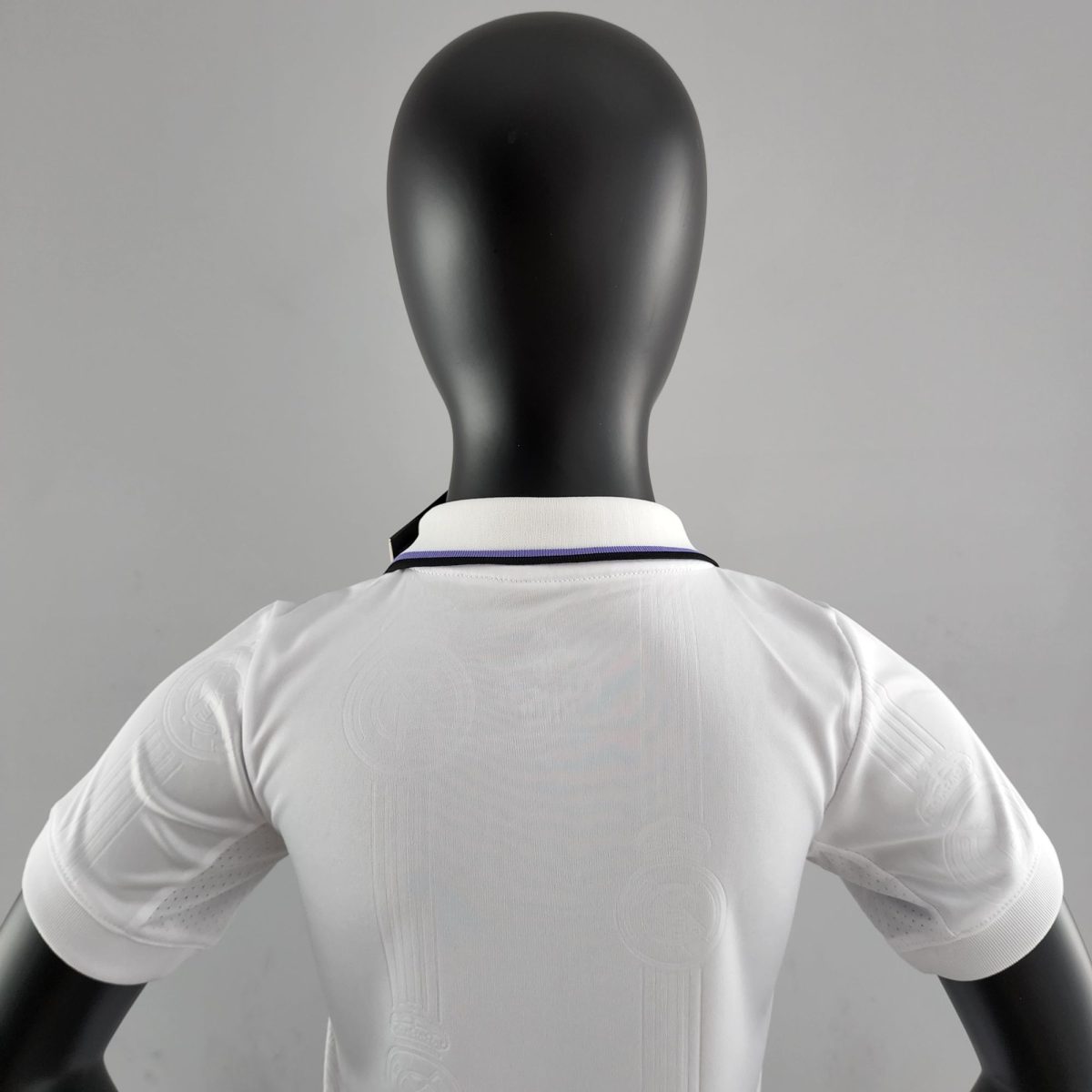 Back view of a black mannequin wearing a white shirt, facing away, with a gray background.