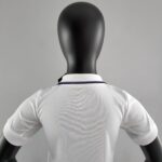 Back view of a black mannequin wearing a white shirt, facing away, with a gray background.