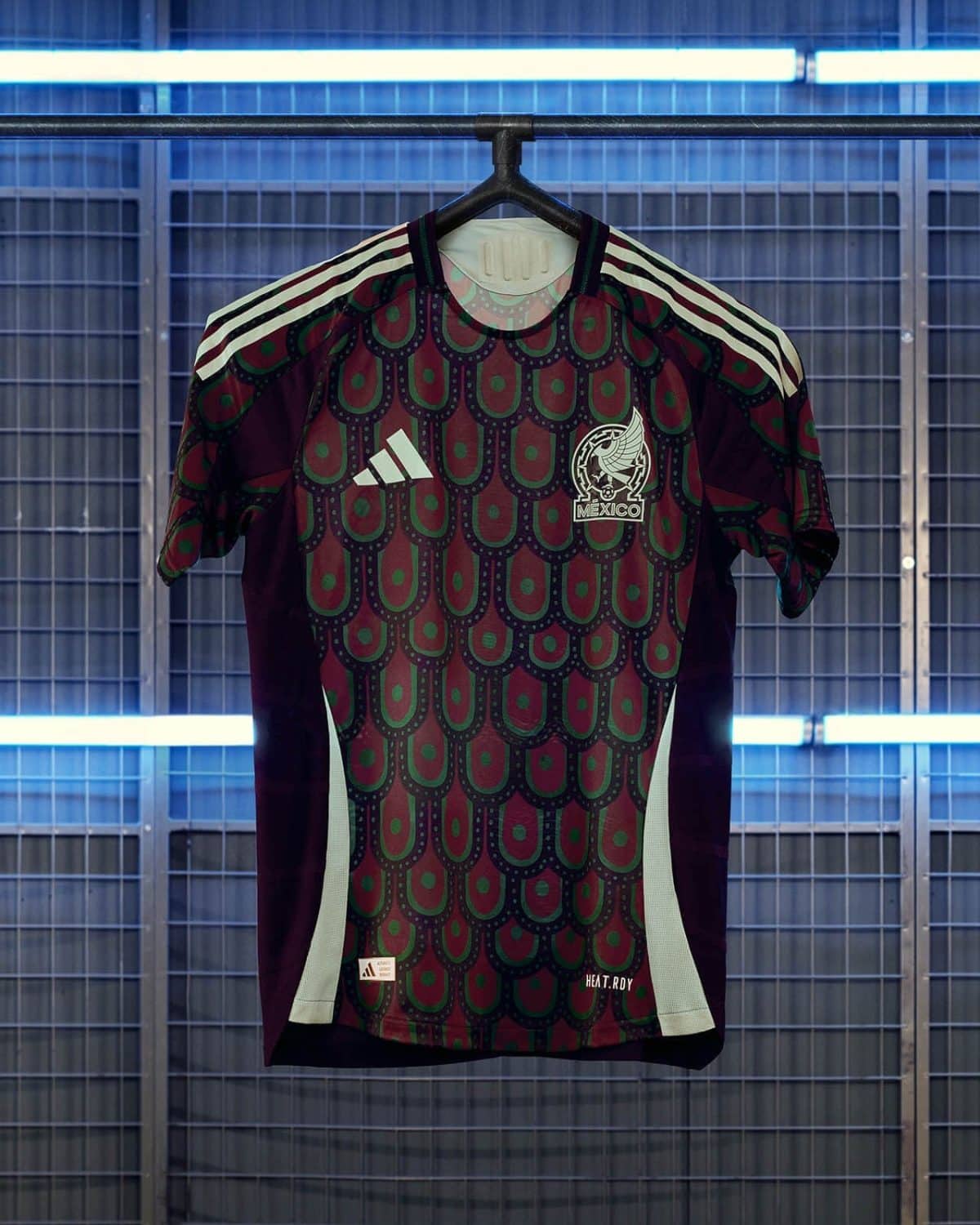 Mexico national team soccer jersey on a hanger with Adidas logo and crest, maroon/green pattern in a blue-lit display