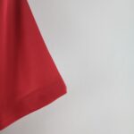 ba085746_fe0e79c4-b676-4ba3-aaac-9c54ae56b9d8 | UAE SPORT STORE Close-up of red fabric with visible stitching along a diagonal edge on a white textured background.
