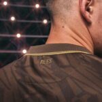 Close-up of a person’s neck and brown patterned jersey with the word 'BEES' on the collar; blurred stadium lights in the background.