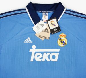 ba58a2de-afb3-44bc-86c7-ce64f0171aeb | UAE SPORT STORE Blue Real Madrid jersey laid flat with official tags and sponsor logo 'TEKA' visible on chest