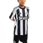 Young boy wearing a black-and-white striped soccer jersey with blue trim and sponsor logo, posing with hands behind back.